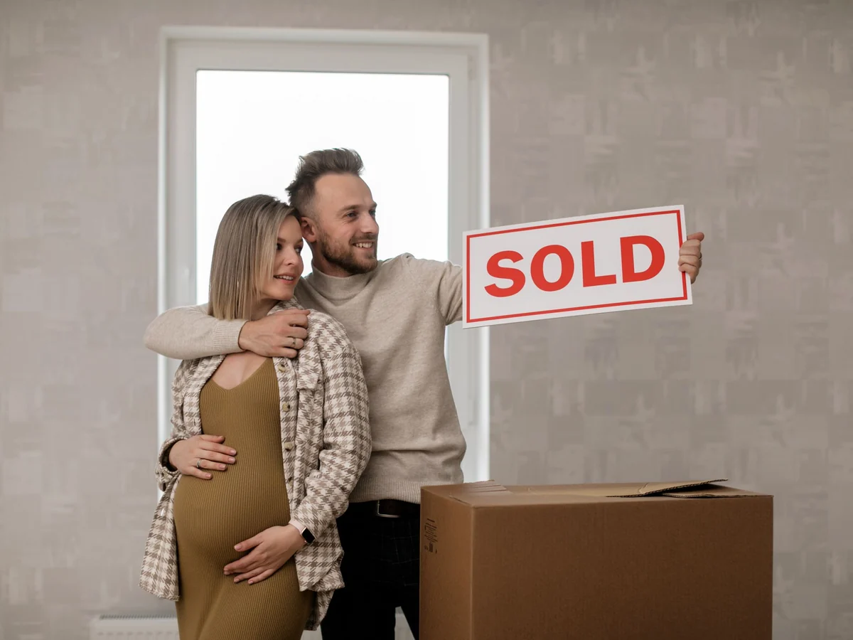 Couple celebrating in front of a sold sign at their new house